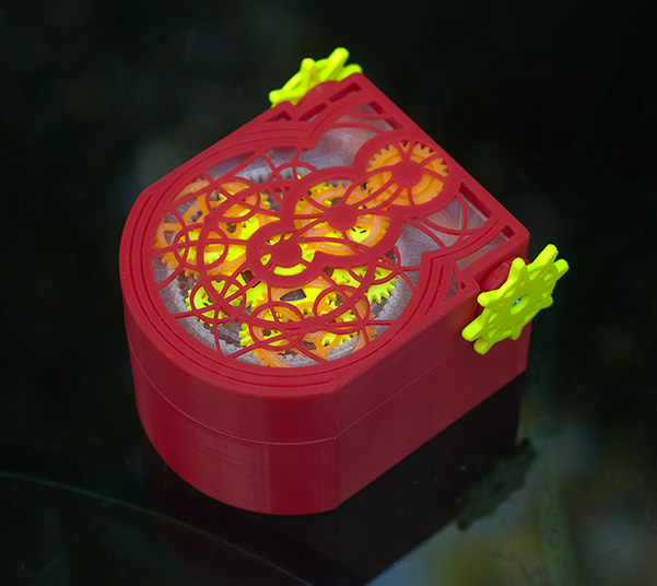 View of the gears through the closed lid - click for larger image closed mechanical box in red, yellow, and orange, showing gears through the holes in the lid
