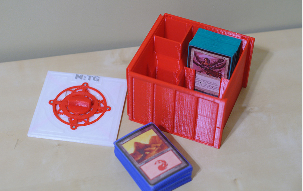 View of an open MTG storage box, which can hold four decks Red and white storage box for Magic: The Gathering with the lid off and a deck of Magic cards inside